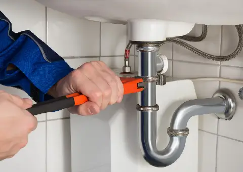 Ervaren loodgieter van Jacolson aan het werk met de waterafvoer en het leidingwerk onder een wastafel.